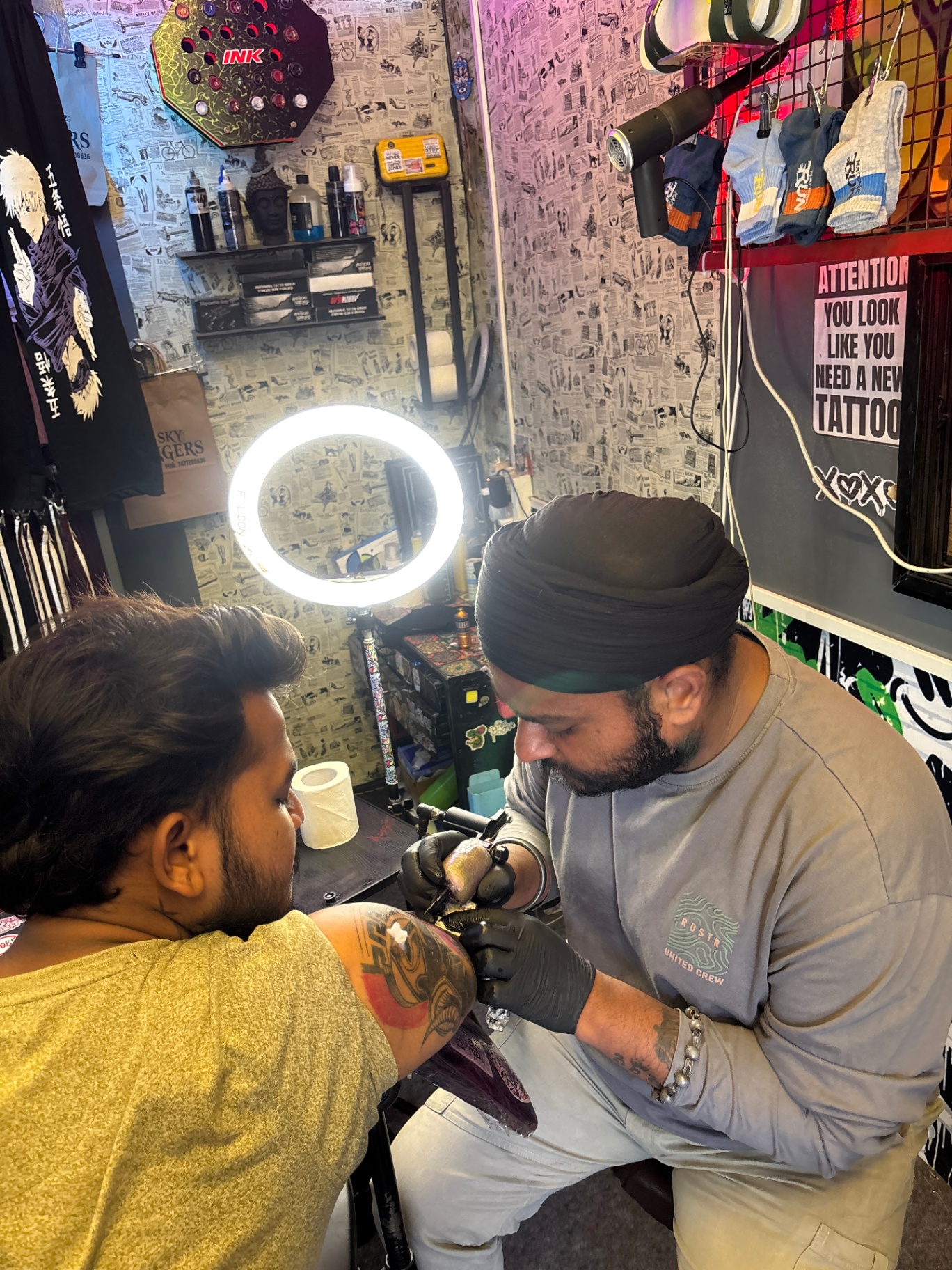 Sky Hangers tattoo — artist tattooing client under ring light